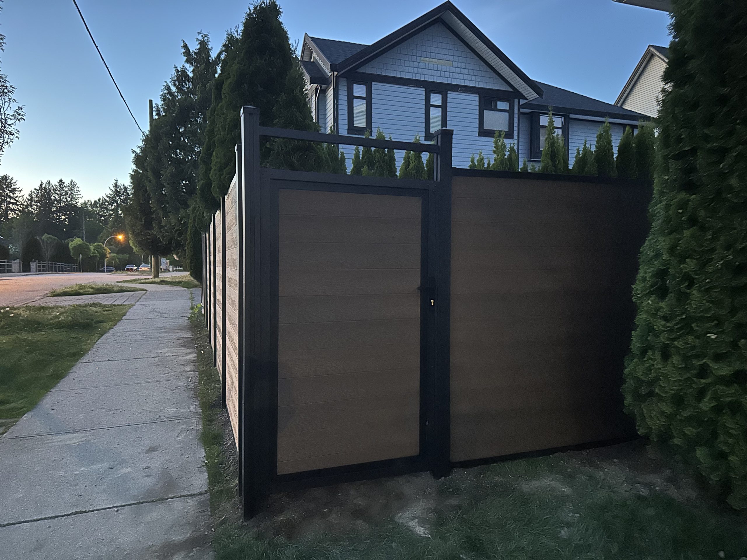 Tall yellow-toned composite privacy fence with custom gate along a Metro Vancouver corner sidewalk