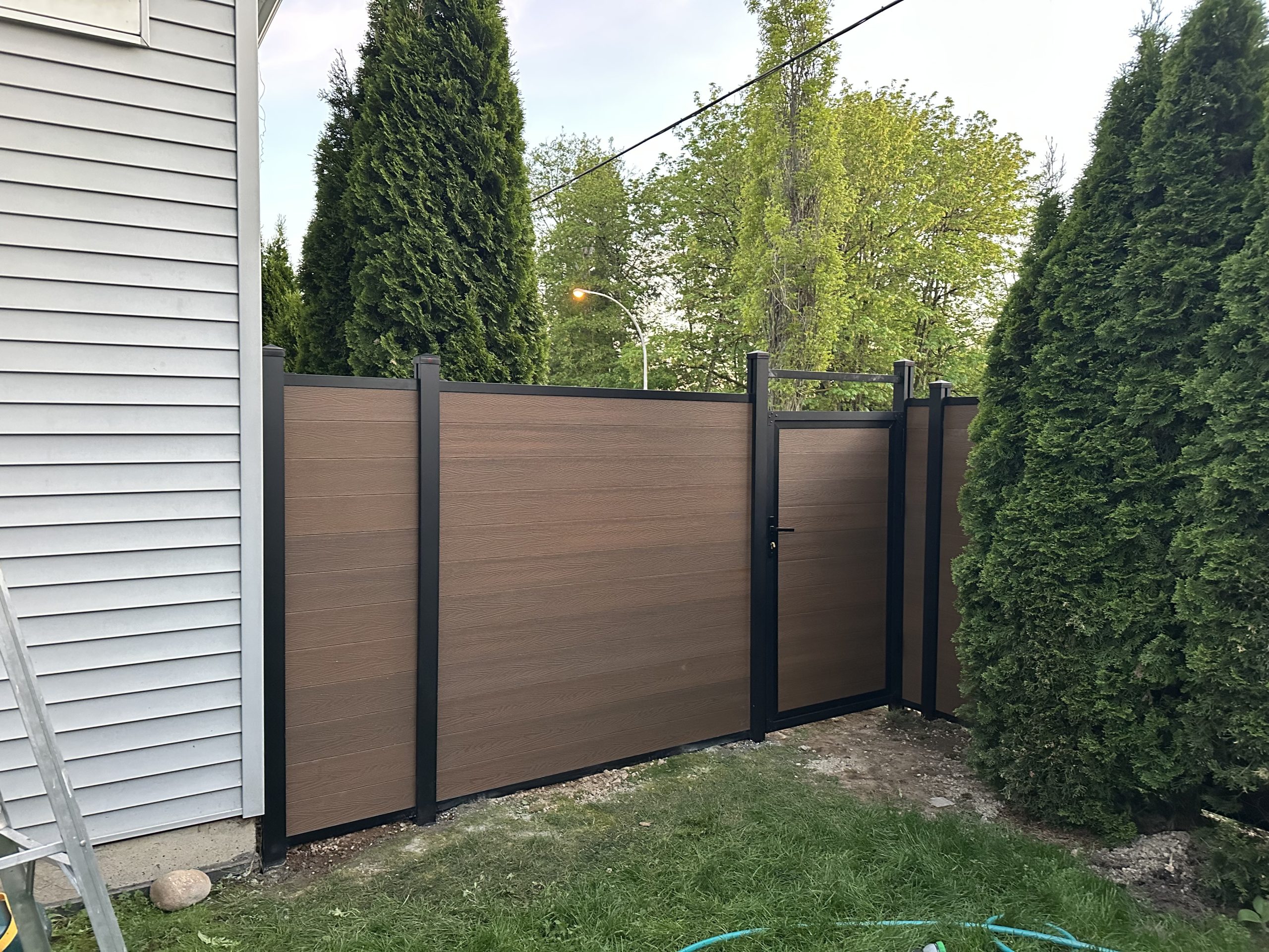 Yellow-toned composite backyard privacy fence with pedestrian gate beside a Metro Vancouver residential home